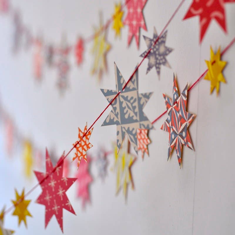 Colourful patterned paper stars threaded onto red string and draped across a pale wall